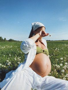 a pregnant woman sitting in a field with dandelions