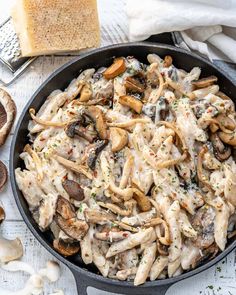 a skillet filled with pasta and mushrooms on top of a white table next to bread