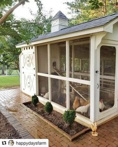 a chicken coop with chickens in it on a brick patio next to trees and grass