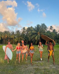 four people walking in the grass with surfboards