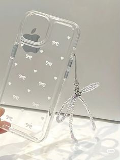 the clear case is holding an apple phone in it's left hand, with white bows and hearts on it