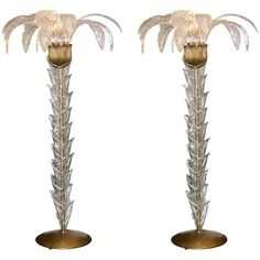 a pair of tall metal and glass lamps with palm trees on each lamp, one is gold