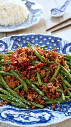 a blue and white plate topped with green beans next to rice on a wooden table