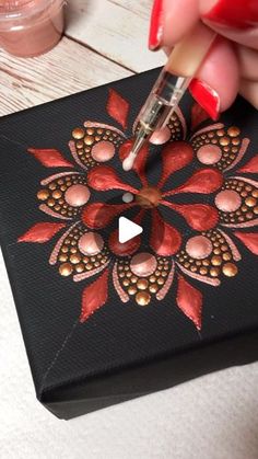 someone is drawing on a piece of black paper with red and gold flowers in the center