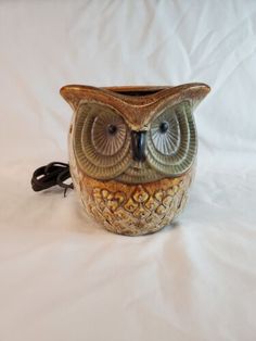 an owl figurine sitting on top of a white sheet covered tablecloth with a black cord