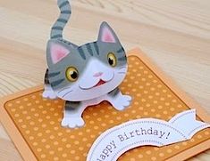 a cat figurine sitting on top of a table next to a sign that says happy birthday