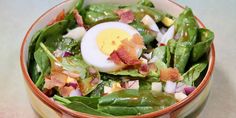 a bowl filled with spinach, bacon and an egg on top of the salad