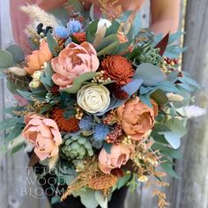 a bridal bouquet with orange, blue and white flowers is held in front of a wooden fence