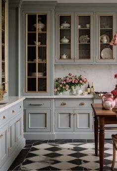 a kitchen with gray cabinets and checkered flooring on the floor, along with pink flowers in vases