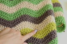 a hand is pointing at a crocheted green and brown blanket on a white surface