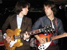 two young men are playing guitars together