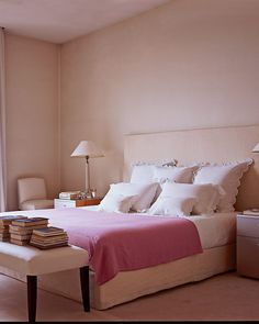 a bed sitting next to a window in a bedroom under a pink blanket and pillows