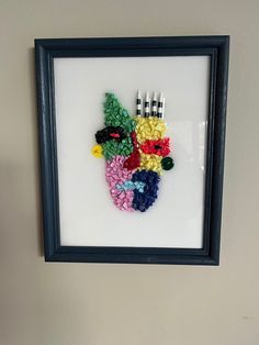 a framed art piece made out of legos and plastic forks on a white wall