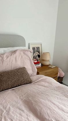 a bed with pink sheets and pillows on top of it next to a night stand