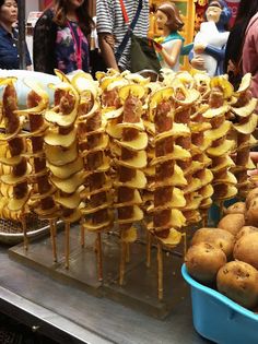 several skewered food items are on display in a market area with people looking at them