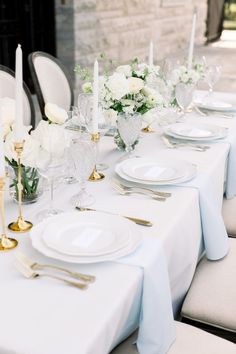 the table is set with white flowers and gold place settings, silverware and candles