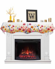 a white fireplace with a flowered tablecloth over the top and fire in it