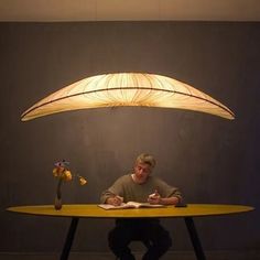 a man sitting at a table with an open book in front of him and a lamp over his head