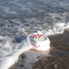 a piece of cake sitting on top of a sandy beach next to the ocean waves