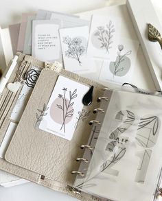 an open planner book with flowers and leaves on it next to some pens and scissors