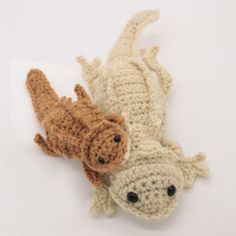 two crocheted dogs laying next to each other on a white surface, one is brown and the other is beige