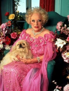 an older woman in a pink dress holding a dog