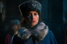 a woman wearing a hat and fur collar in a dark room with other people around her