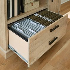 an open file cabinet with files and folders in the bottom drawer, on wooden flooring