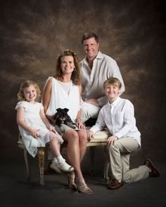 a family posing for a portrait with their dog and two children in front of a dark background