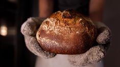 a close up of a person holding a loaf of bread in their hands and wearing gloves