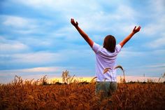 a person standing in a wheat field with their arms up and hands raised above their head