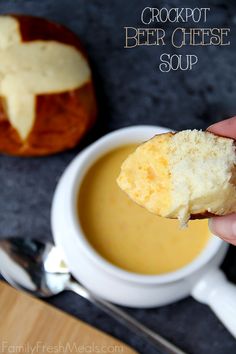 a hand holding a piece of bread over a cup of soup