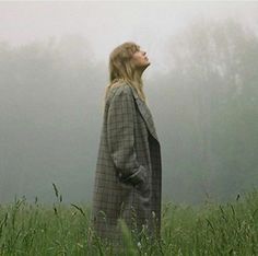 a woman standing in tall grass looking up into the sky