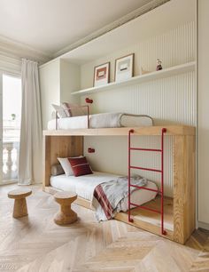 two bunk beds in a room with wooden floors and white walls, one has a red ladder