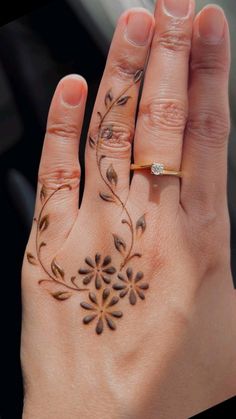 a woman's hand with a ring and flower tattoo on her left hand,