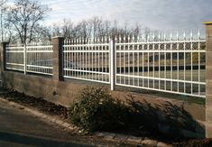 a white picket fence on the side of a road next to a tree and bushes