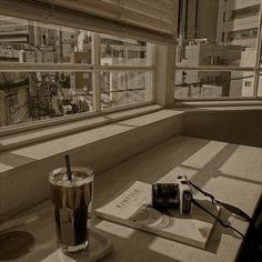 a table with a book, camera and drink on it in front of a window