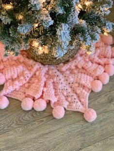 a crocheted pink pom - pom blanket sits next to a potted christmas tree