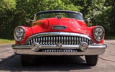 an old red car parked on the side of the road in front of some trees