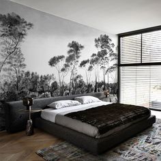 a large bed sitting in the middle of a bedroom next to a wall with trees on it