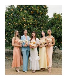 a group of women standing next to each other in front of an orange tree holding bouquets