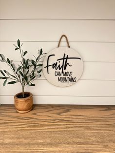 a sign that says faith can move mountains next to a potted plant on a table