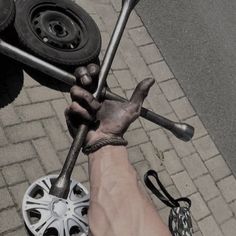 a person holding two wrenches in their hand on the ground next to a tire