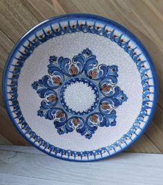 a decorative blue and white plate sitting on top of a wooden table next to a wall