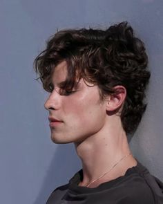 a close up of a person with curly hair wearing a gray shirt and looking off to the side