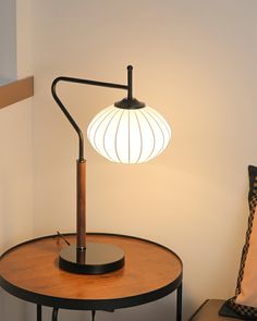 a table lamp sitting on top of a round wooden table next to a white wall