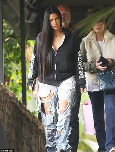 a woman in ripped jeans walking down the street with a man behind her and another person looking on