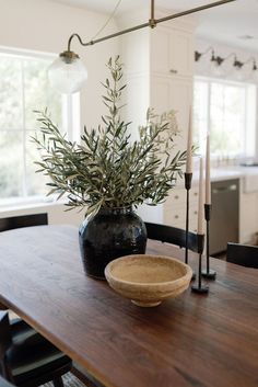 a wooden table topped with a black vase filled with greenery next to a candle