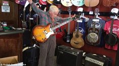 an older man is playing the guitar in his music store with other guitars and amps behind him