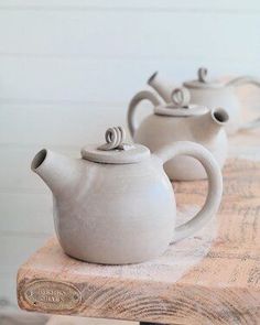 three white teapots sitting on top of a wooden table next to each other